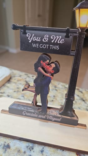 Customer's personalized wooden plaque of a couple kissing under a lamppost with the names 'Graciela and Miguel' on the base.