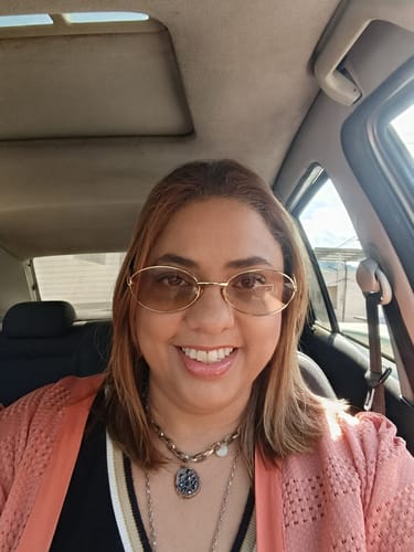 Cliente sorrindo em um carro usando os Óculos Corfu com armação fina e lentes claras.