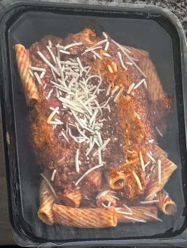 Customer's Fit Turkey Pasta in a black container, showing rigatoni with meat sauce and shredded cheese.