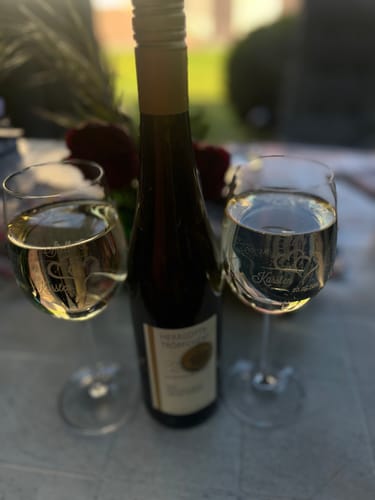 Rezensent zeigt die gravierten Leonardo Weingläser 'Die Große Liebe' mit Weißwein auf einem Tisch.
