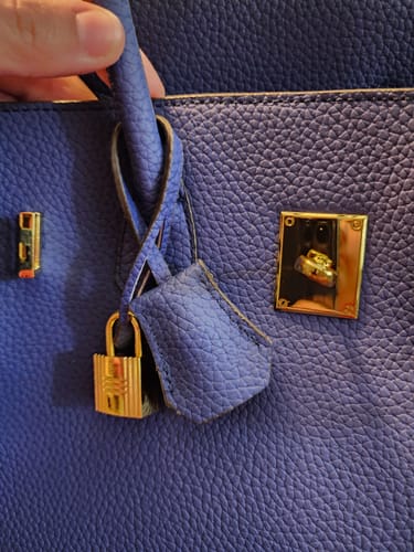 Close-up of a reviewer's blue Warkin Bag, showing the pebbled leather and gold lock-style closure.