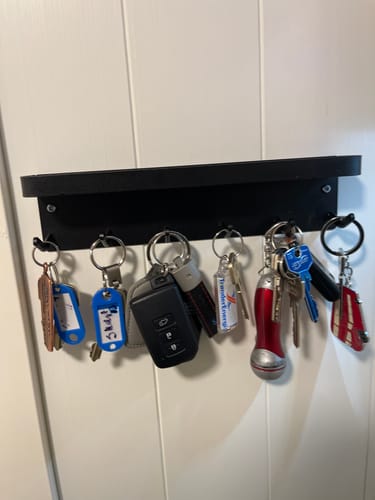 Kundens svarte selvklebende nøkkelholder montert på en hvit vegg med flere nøkkelknipper.