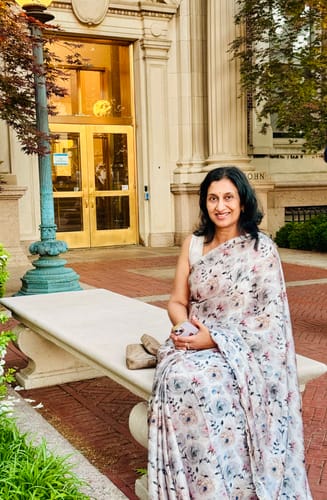 Reviewer sitting outdoors on a bench wearing the floral print Satin Georgette Silk Saree.