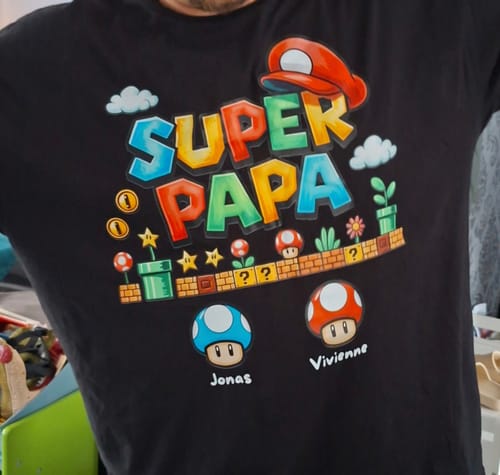Ein Kunde trägt das personalisierte, schwarze Super Papa T-Shirt mit farbenfrohem Videospiel-Aufdruck.