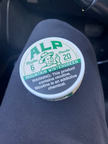 Customer's round, white tin of ALP Mountain Wintergreen Nicotine Pouches resting on their lap.