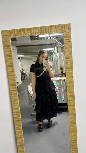 Cliente tira uma selfie no espelho usando a Alça Aurora creme na transversal sobre uma roupa preta.