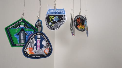 Reviewer's triangular Starship Flight 12 Collectors Patch hanging in a collection of other embroidered space patches.