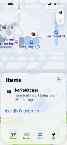 Reviewer's screenshot of the Find My app showing the SPOTMINDERS tracking card locating a lost suitcase at an airport terminal.
