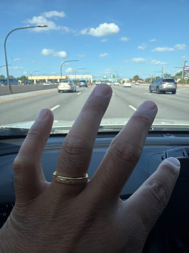 Customer's hand wearing the gold Aureum ring with a sandblasted texture, taken from inside a car on a highway.