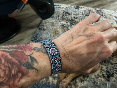 Customer wearing the Grieving Is A Process Bracelet, which features a detailed blue, pink, and black floral pattern.