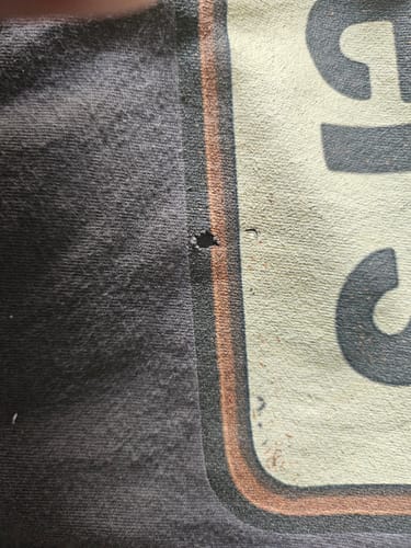 Close-up of the reviewer's Clowns or Jokers T-Shirt, showing a small hole in the dark fabric next to the graphic.