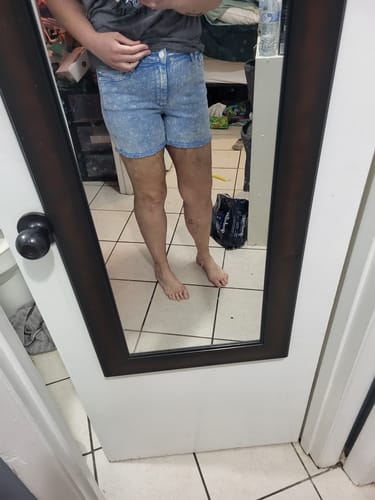 Reviewer taking a mirror selfie to show the fit of the mid-rise cyan denim shorts.
