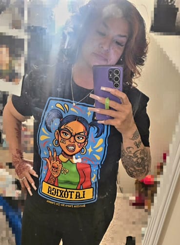 Reviewer taking a mirror selfie wearing the black La Toxica Loteria Tee, showing the colorful graphic.