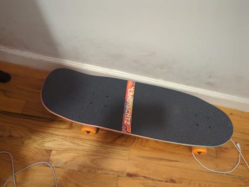 Customer's Landyachtz Tugboat Nightfall longboard on a hardwood floor, showing the top grip tape and orange wheels.