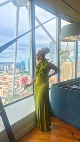 Reviewer looking out a window while wearing the full-length green Naked Ruffle Halter Maxi Dress.