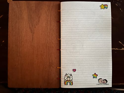 A customer's open wooden notebook with a lined page decorated with cute character stickers from the subscription.