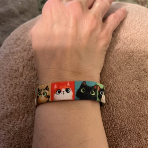 Close-up of a customer's wrist wearing the colorful Who Me? Cat Bracelet, which features cartoon cat faces.