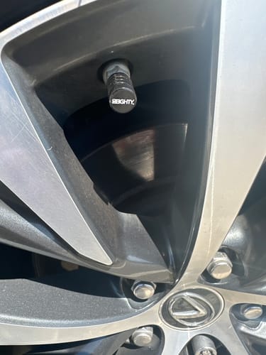 Close-up of a customer's black 80Eighty Valve Stem Cap installed on a car wheel.