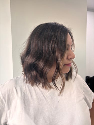 Clienta de perfil con cabello castaño ondulado, mostrando el brillo del tratamiento de Polvo de Cassia.