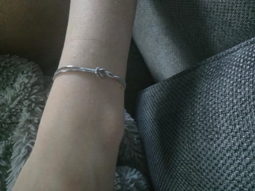A customer's wrist wearing the silver Forever Knot Bracelet while sitting on a couch.
