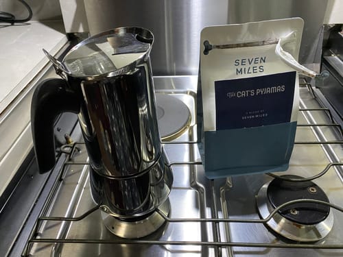 Customer's bag of The Cat's Pyjamas coffee next to a moka pot on a compact gas stove.