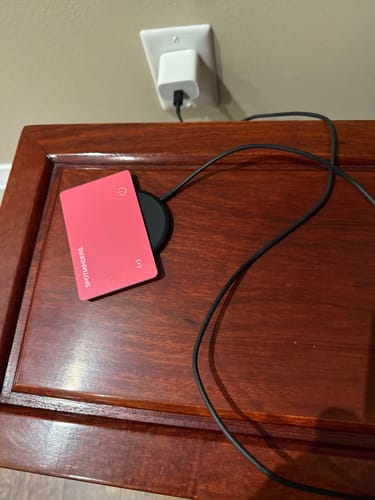 Customer's black Magnetic Wireless charger on a wooden table, charging a pink tracking card.