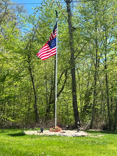 Customer's historic American flag flying on a flagpole in a grassy yard with trees in the background.