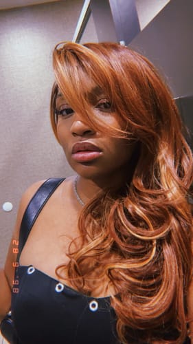 Reviewer wearing the long, wavy Outre Kihara wig, showing its reddish-brown color with blonde highlights.