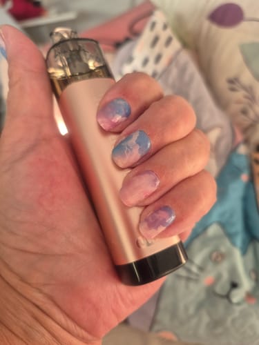 Nahaufnahme der Hand einer Kundin mit den UV Gel Nagelfolien 'Rainbow Vision' im pastellfarbenen Wolkendesign.