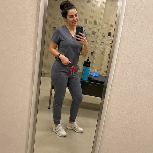 Reviewer in scrubs wearing their white Novera™ sneakers in a locker room.