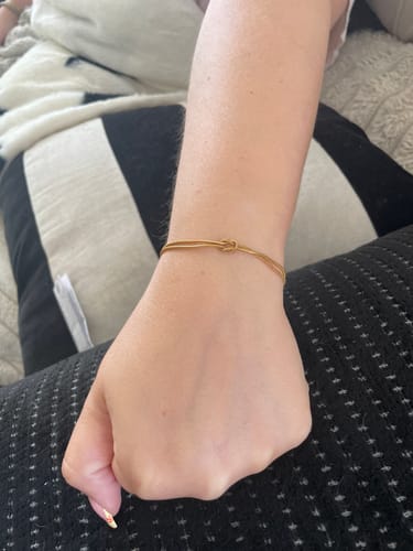 Customer wearing the delicate gold Forever Knot Bracelet on their wrist, showing the knot detail.