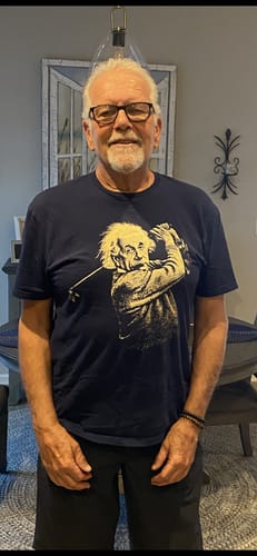 Reviewer standing indoors wearing the dark Einstein Teeing Off 6 T-Shirt, showing the fit and graphic.