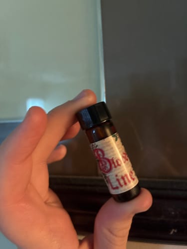 Customer's hand holding a small amber vial of Bloodline Oil.