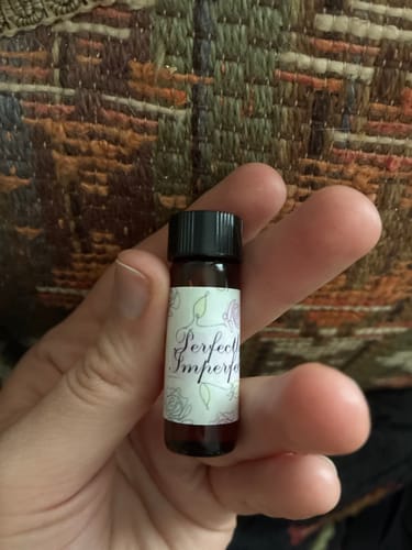 Customer holding a small vial of Perfectly Imperfect Oil Dram against a textured background.