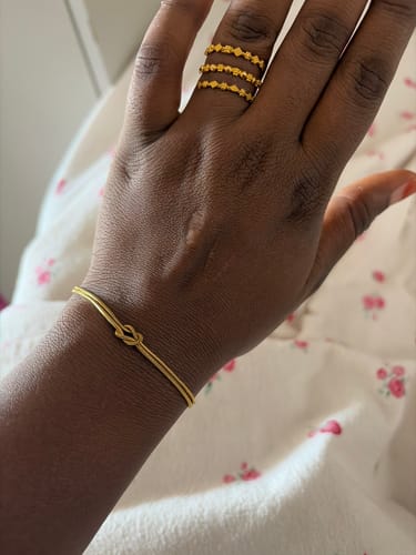 Reviewer's hand wearing a delicate gold knot bracelet and a stacked ring.