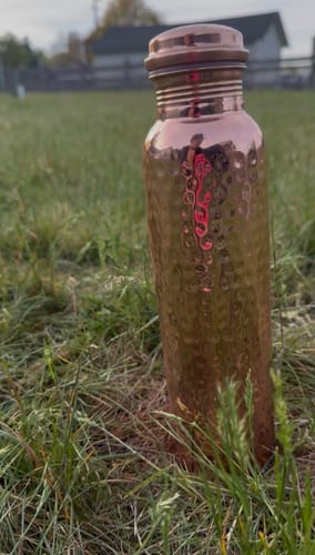 Customer's Himalayan Ayurvedic Copper Bottle with a hammered texture, standing in a grassy field.