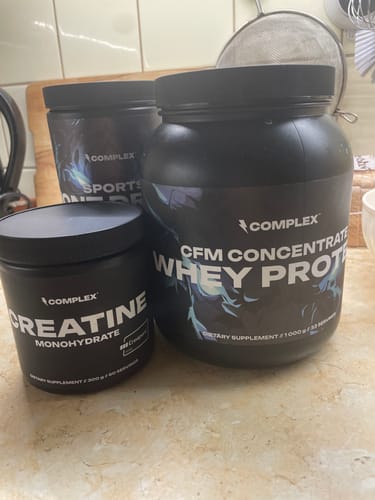 Reviewer's black tubs of CFM Whey Protein and Creatine Monohydrate sitting on a kitchen counter.