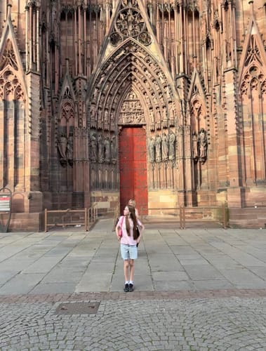 Reviewer from behind wearing the pink swan song baby tee in front of a large cathedral.