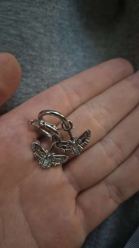 Reviewer holding the pair of detailed, silver Moth Dangle Earrings in their open palm.