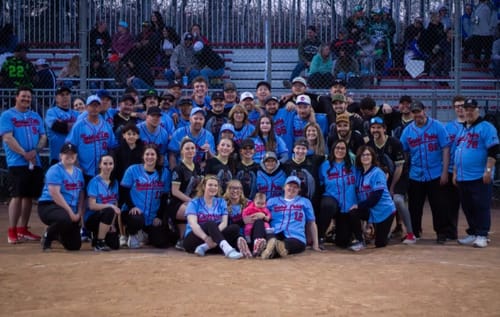 Customer's family teams posing on a baseball field at night in their light blue custom jerseys.