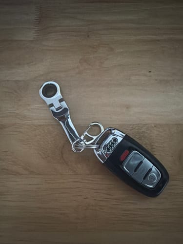 Customer's silver 10mm Wrench Keychain attached to a black Audi car key, resting on a wooden surface.