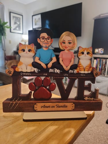 Customer's personalized wooden plaque showing cartoon figures of a couple and two cats sitting atop the word 'LOVE' on a table.