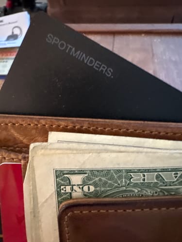 A customer's black SPOTMINDERS tracking card fitting neatly into a wallet with cash.