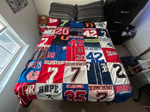 Customer's Project Repat T-Shirt Quilt made from colorful sports jerseys spread across a bed in a bedroom.