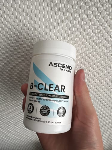 Customer holds the white bottle of B-CLEAR skin control supplements.