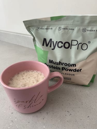 Reviewer's smooth MycoPro drink in a pink mug, with the mushroom protein powder packaging in the background.