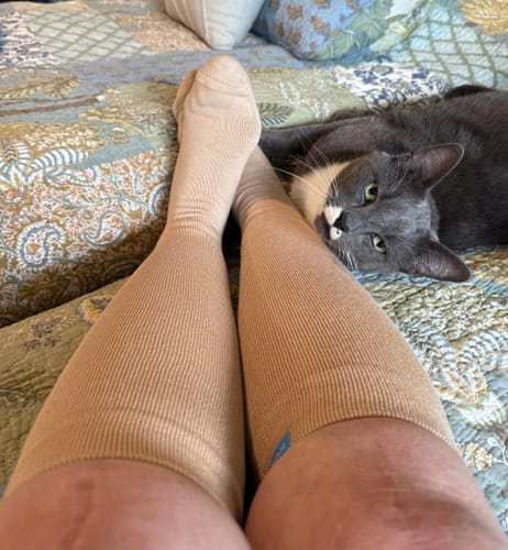 Reviewer wearing beige Eucalyptus Lyocell Compression Socks while relaxing on a bed with a cat.