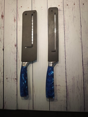 Ein Kunde zeigt zwei Messer mit blauen Griffen in schwarzen Schutzhüllen an einer Wand.
