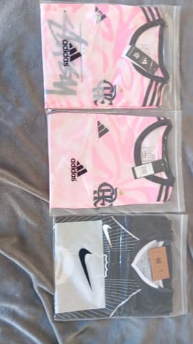 Client montrant deux maillots roses spéciaux Flamengo 24/25 et un autre maillot, tous pliés dans leur emballage.
