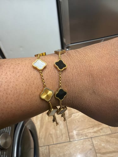 Reviewer showing two Celine Clover Bracelets on their wrist with white, black, and textured gold charms.